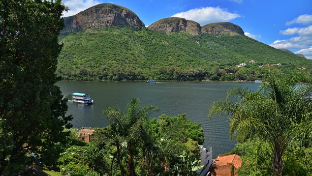A lake with a boat, surrounded by lush greenery and mountains. - The Shore House (Hartbeespoort)