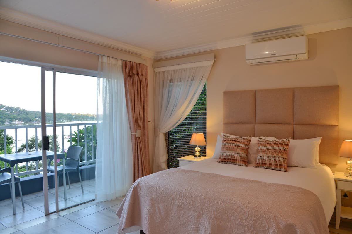 A hotel room with a large bed, a balcony with a table and chairs, and a view of a body of water.