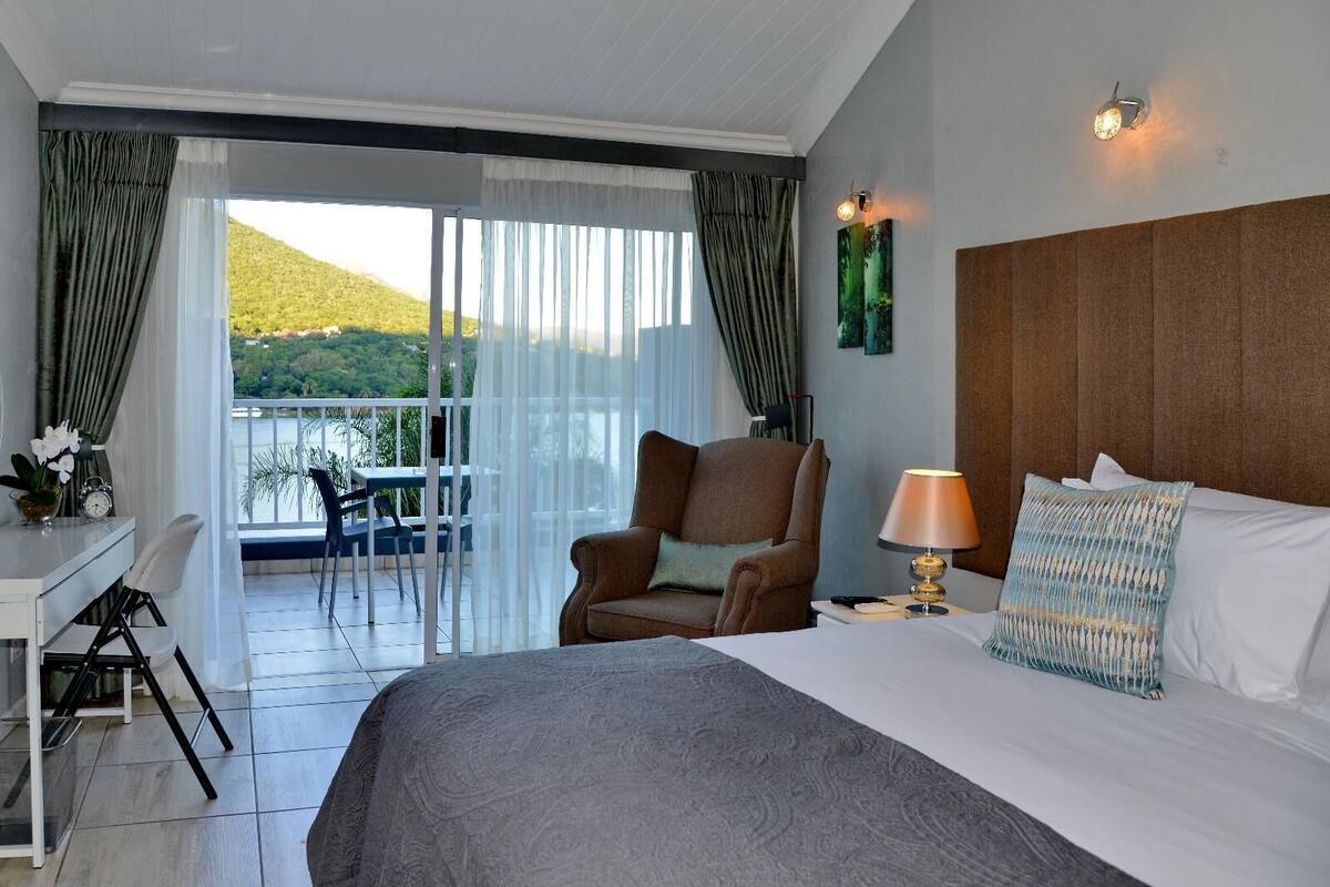 A hotel room with a bed, a chair, a desk, and a view of a balcony with a table and chairs.