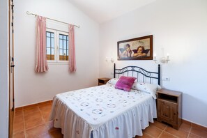 Une chambre à coucher avec un lit, une table de chevet, un tableau accroché au mur et une fenêtre avec des rideaux.