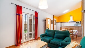 A living room with a green sofa, a wooden table, and a kitchen area with a white stove. - Rustic Home Close to Beach with Pool, Terrace, Garden & Wi-Fi; Pets Allowed, Parking Available (Conil de la Frontera)