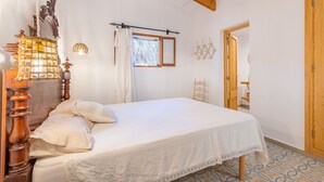 Een slaapkamer met een houten bed, een hanglamp, een raam met gordijnen en een houten garderobekast.