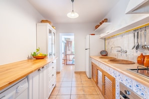 A kitchen with white cabinets, a wooden countertop, a sink, and a hanging utensil rack.