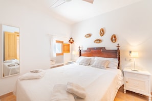 A bedroom with a wooden headboard, a large mirror, a bedside table with a lamp, and a neatly made bed with pillows and a folded towel.
