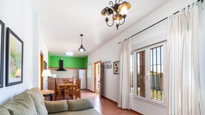 Un soggiorno con divano, tavolo da pranzo e sedie, una cucina con parete verde e un'ampia finestra con tende.
