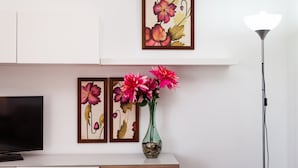 Una TV a schermo piatto, un vaso con fiori e delle opere d'arte incorniciate su una parete.