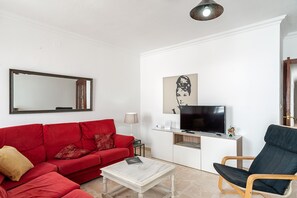 A living room with a red sofa, a black chair, a white coffee table, a TV, and a mirror on the wall. - Central Apartment Close to Beach with Optical fibre & Terrace; Pets Allowed (Conil de la Frontera)