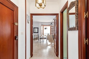 A hallway leading to a dining area with a table and chairs, a chandelier, and a mirror on the wall.