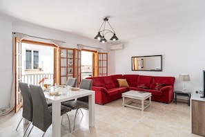 Un salon avec un canapé rouge, une table à manger blanche avec des chaises, une table basse et un meuble pour la télévision.