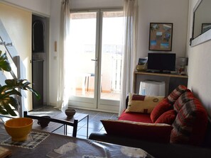 Uma sala de estar pequena com um sofá, uma mesa com uma tigela, uma televisão e uma porta de vidro corria para uma área externa.