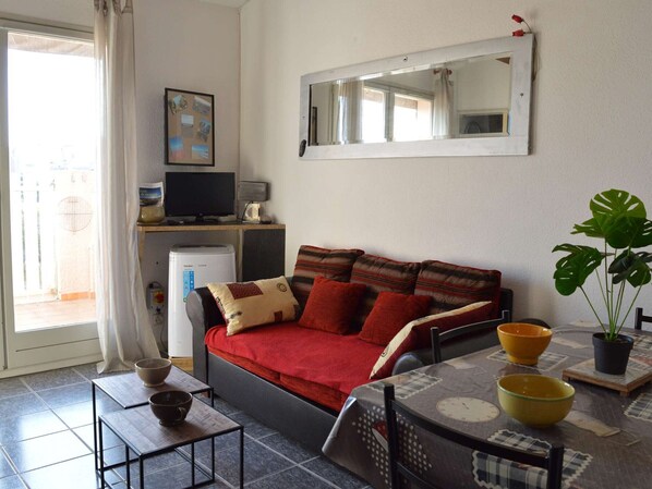 Um espaço compacto para viver, com um sofá, uma mesa pequena, uma televisão e uma planta em vaso.
