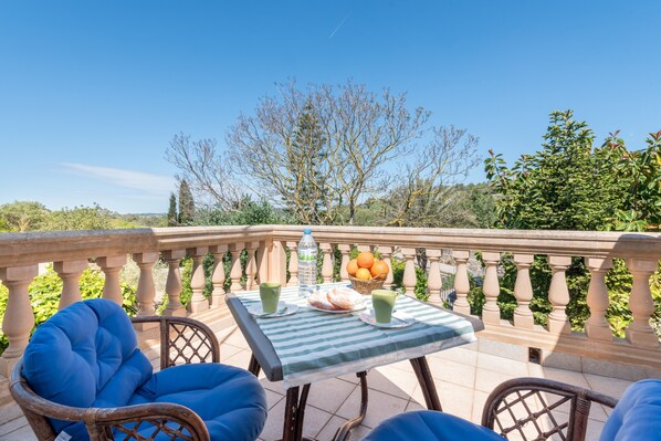 Une terrasse avec des chaises en osier, une table recouverte d’une nappe à rayures et un panier rempli d’oranges.