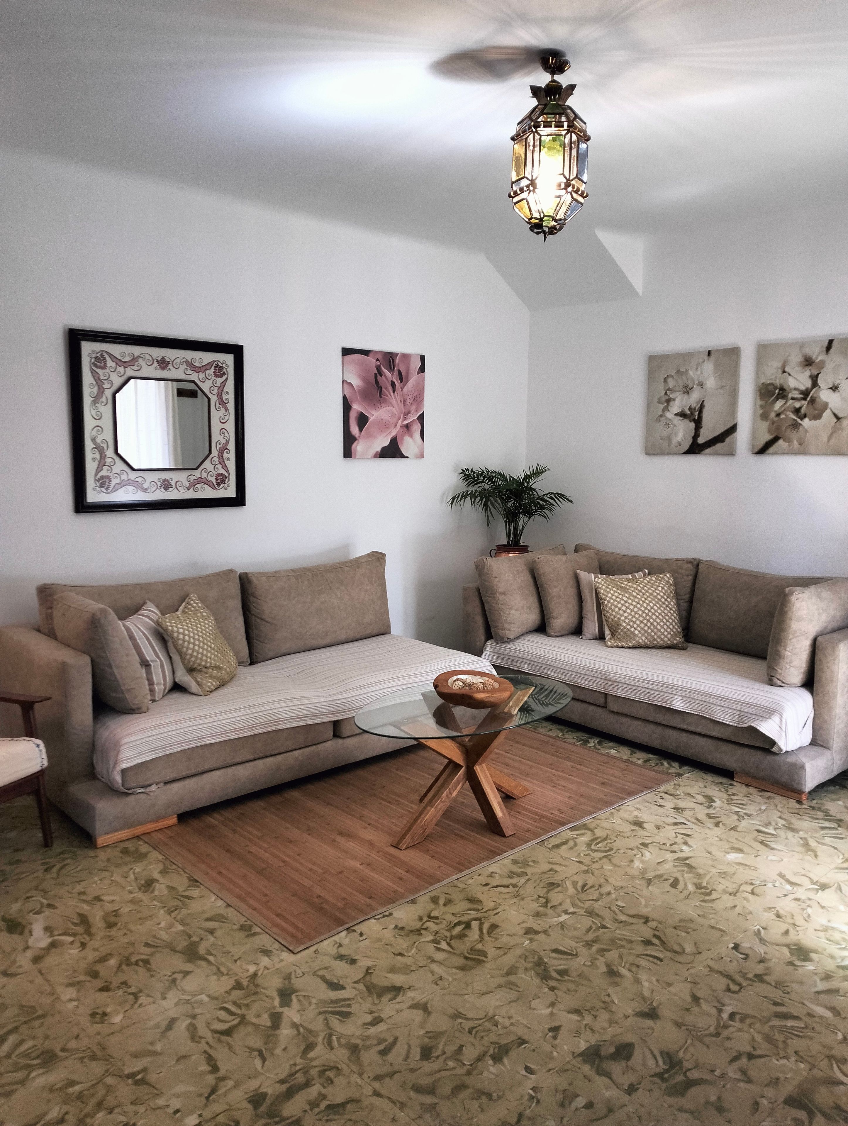 A living room with a sofa, a glass coffee table, a mirror, and wall art.