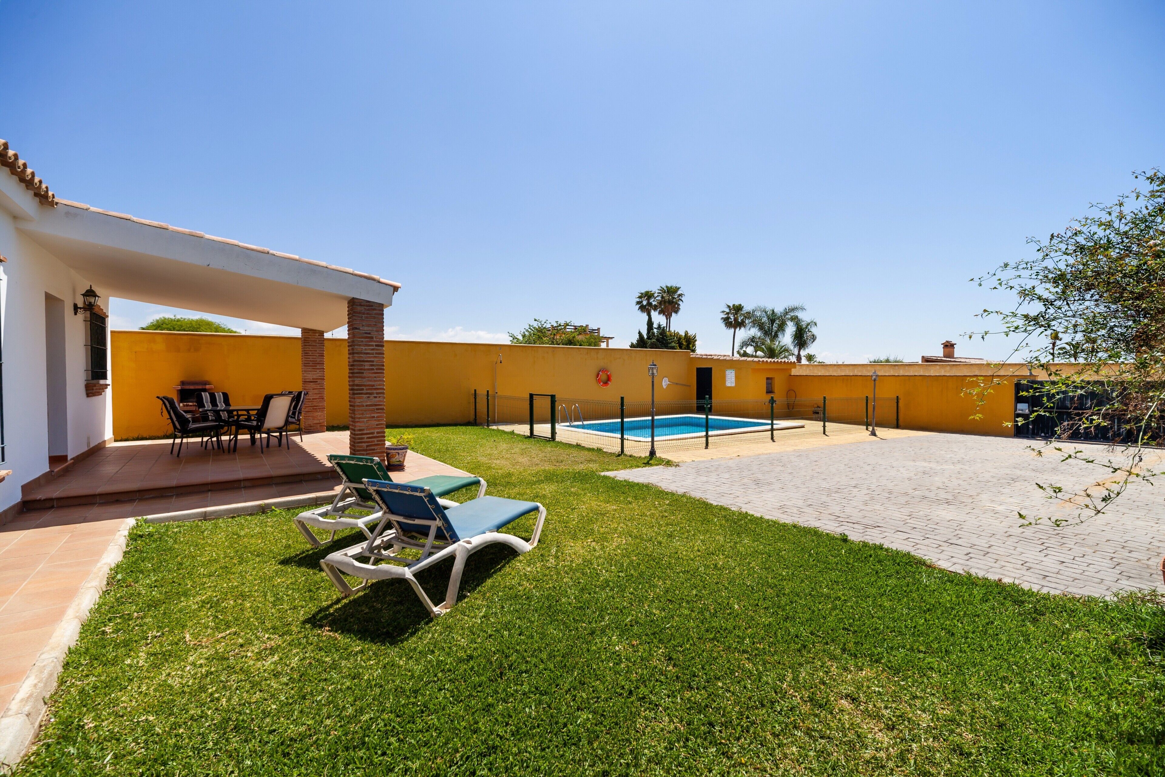 A backyard with a pool, patio furniture, and a covered seating area.