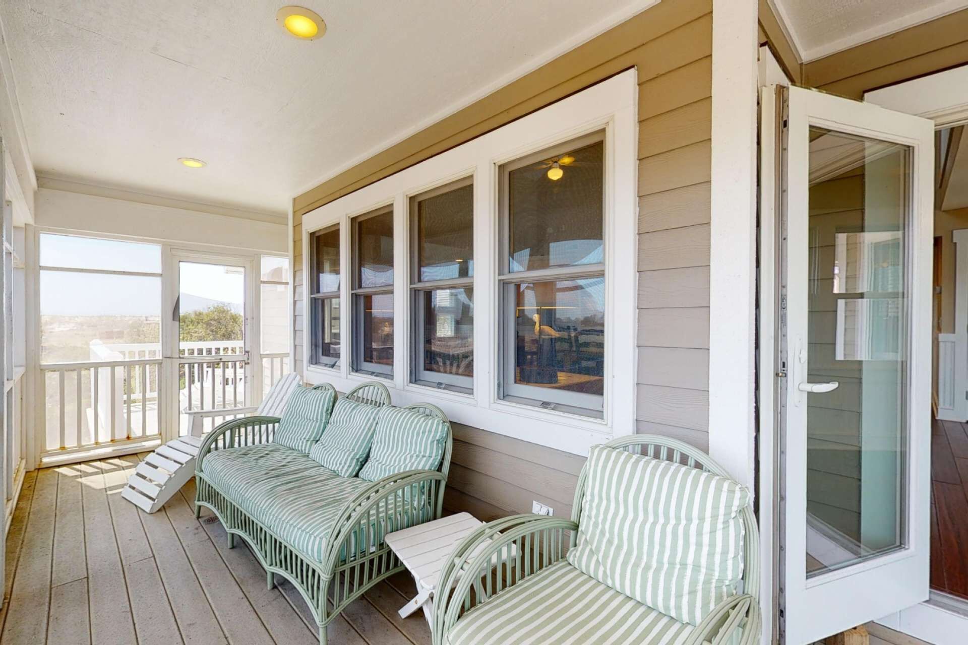 A covered porch with wicker furniture and large windows.