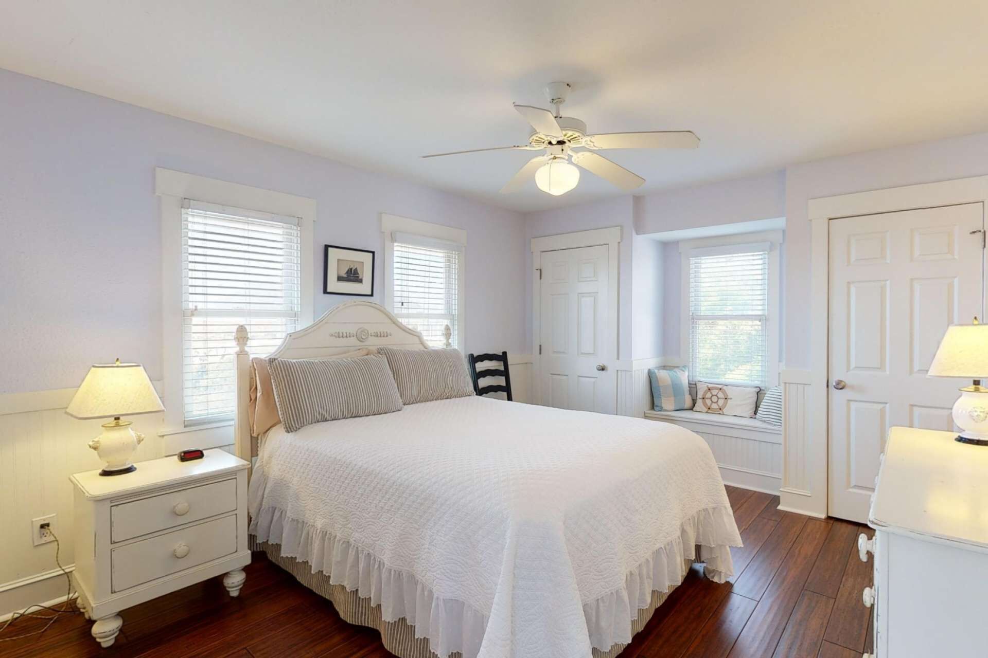 A bedroom with a bed, nightstands, a ceiling fan, and windows with blinds.