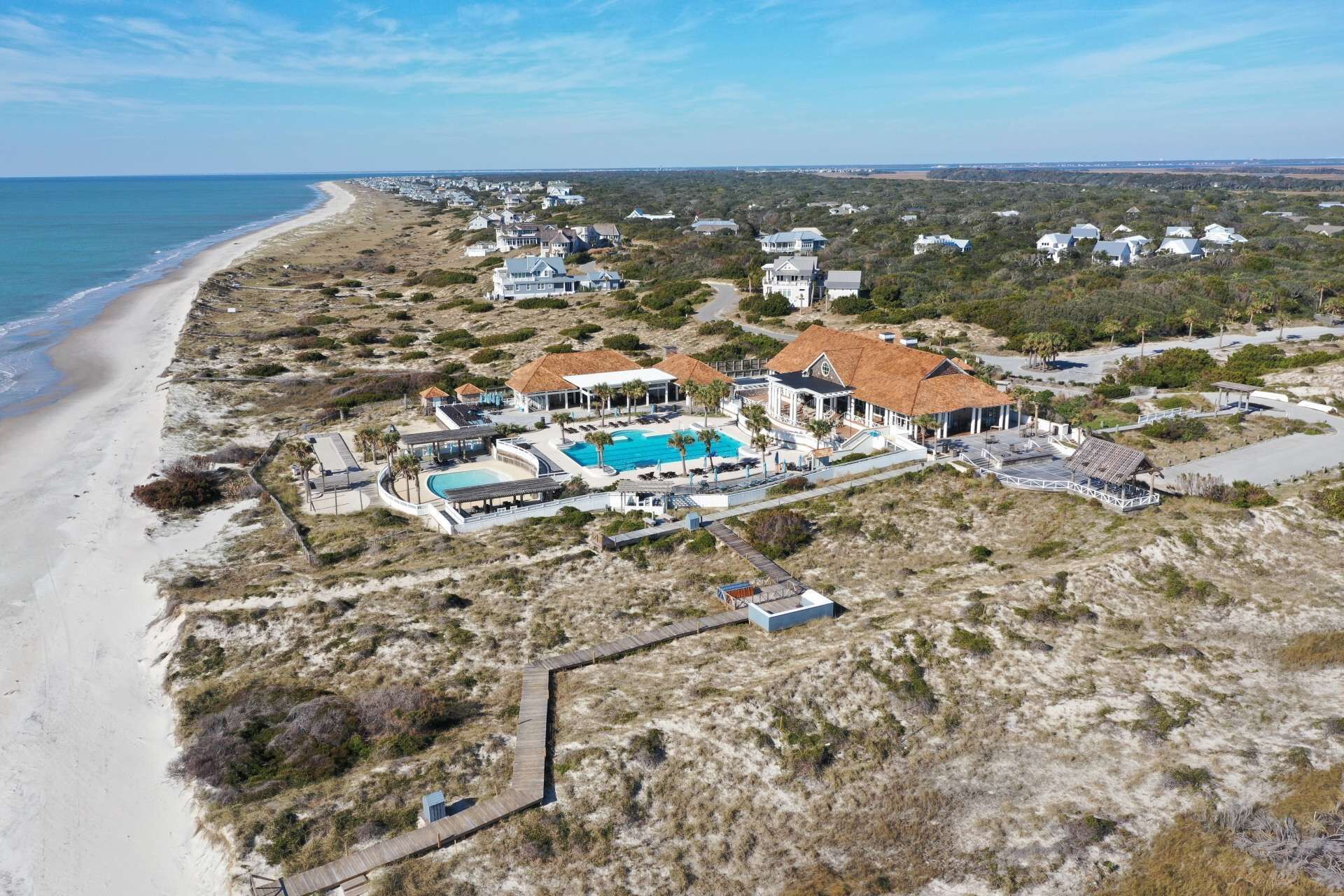 Vue aérienne d’une propriété située sur la côte, avec une grande piscine, plusieurs maisons et une plage.