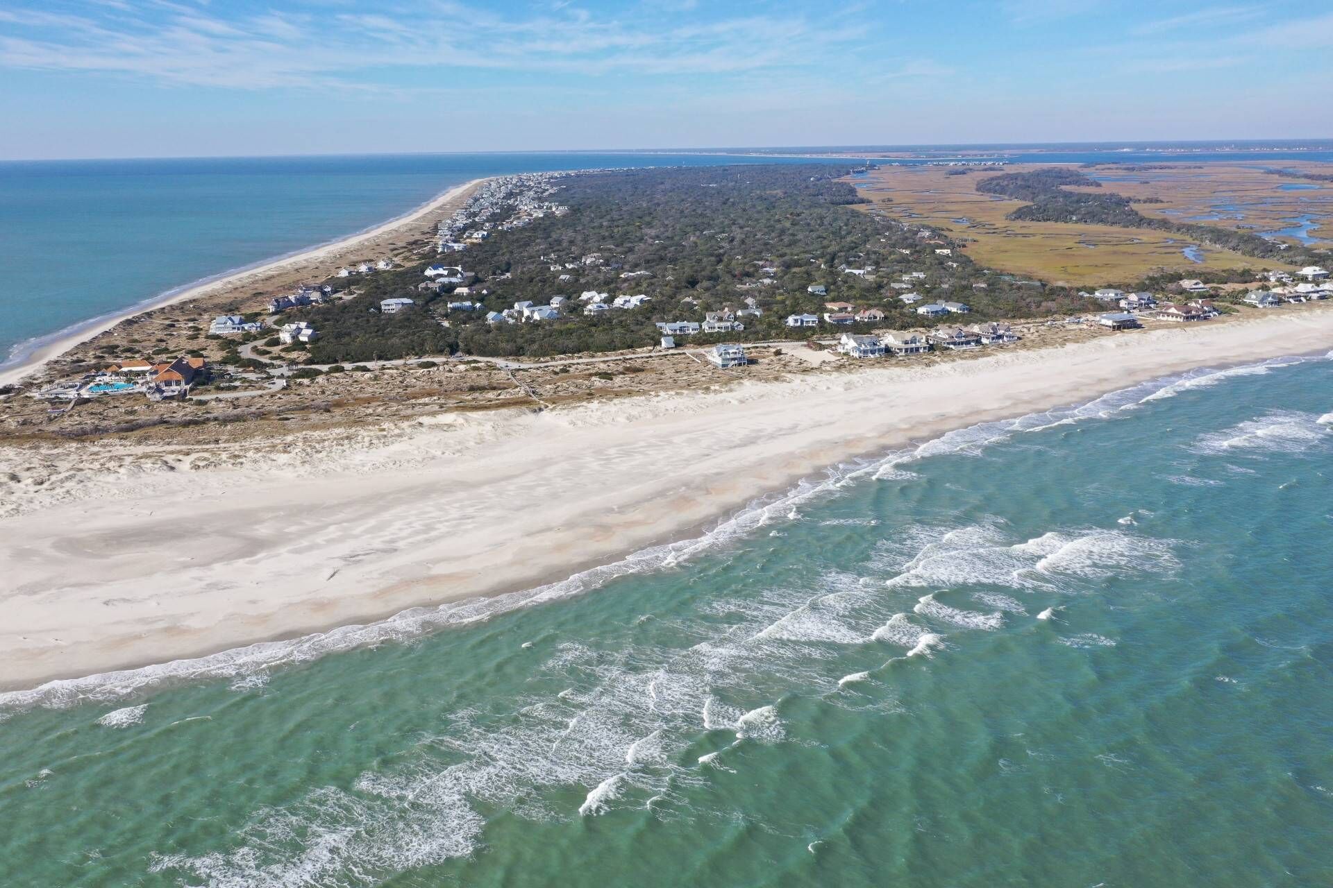 Ein Luftbild einer Küstenregion mit Strand, Häusern und einem bewaldeten Hügel.