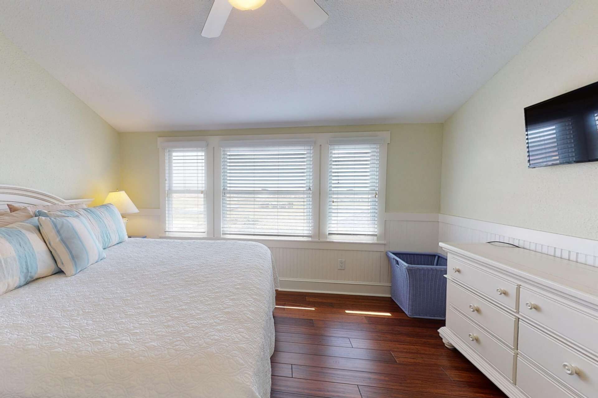 A bedroom with a bed, a dresser, a window with blinds, and a ceiling fan.
