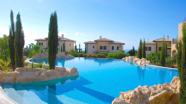 Una amplia piscina rodeada de villas de estilo mediterráneo con vista despejada al mar.