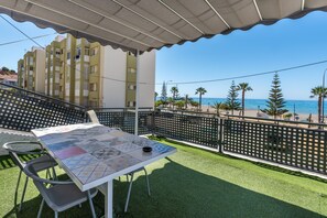Un balcon avec une table et des chaises, donnant sur une plage et des immeubles.