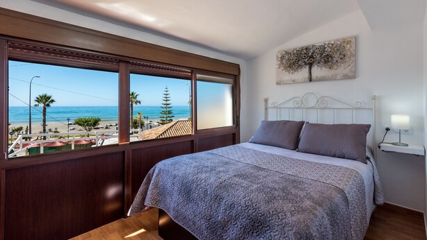 A bedroom with a large window, a bed, a bedside table, and a wall-mounted artwork. - Beachfront Apartment with Air Conditioning, Stunning Views, Terrace, and Wi-Fi (Benajarafe)