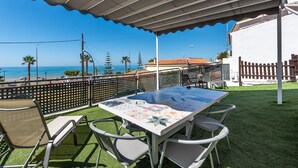An outdoor patio with a table and chairs, a view of the sea, and a white building in the background. - Beachfront Apartment with Air Conditioning, Stunning Views, Terrace, and Wi-Fi (Benajarafe)