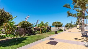 A paved walkway with palm trees and a clear blue sky. - Beachfront Apartment with Air Conditioning, Stunning Views, Terrace, and Wi-Fi (Benajarafe)