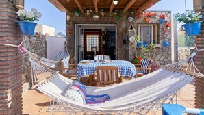 Un espacio de estar al aire libre cubierto con una hamaca, pared de piedra y plantas en macetas.