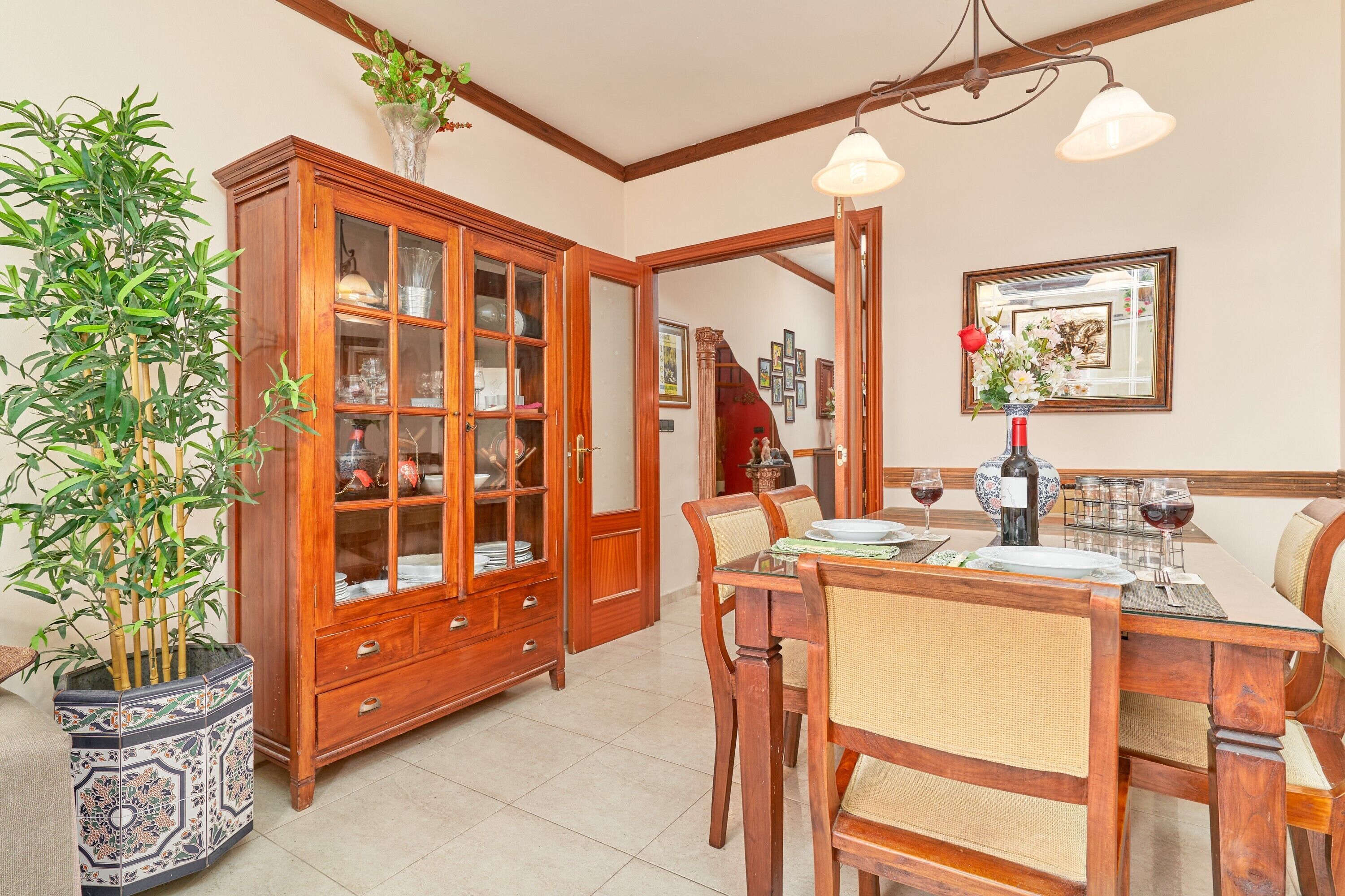 A dining area with a wooden cabinet, a dining table set for four, and a potted plant.