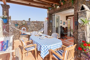 A patio with a checkered tablecloth, wooden chairs, a hammock, and a stone wall with decorative plates. - Air-Conditioned Apartment Close to Beaches with Rooftop Terrace (Nerja)