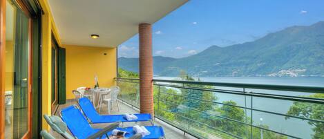 A balcony with blue chairs and a table, overlooking a lake and mountains.