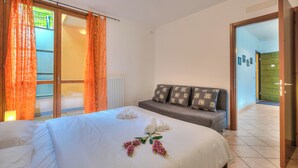 Una camera d'albergo con un letto, una divano e una porta scorrevole in vetro che dà su un balcone.