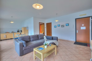 A living room with a sofa, a coffee table, and a kitchen area in the background. - Va Pensiero sul lago Stunning View (Tronzano Lago Maggiore)