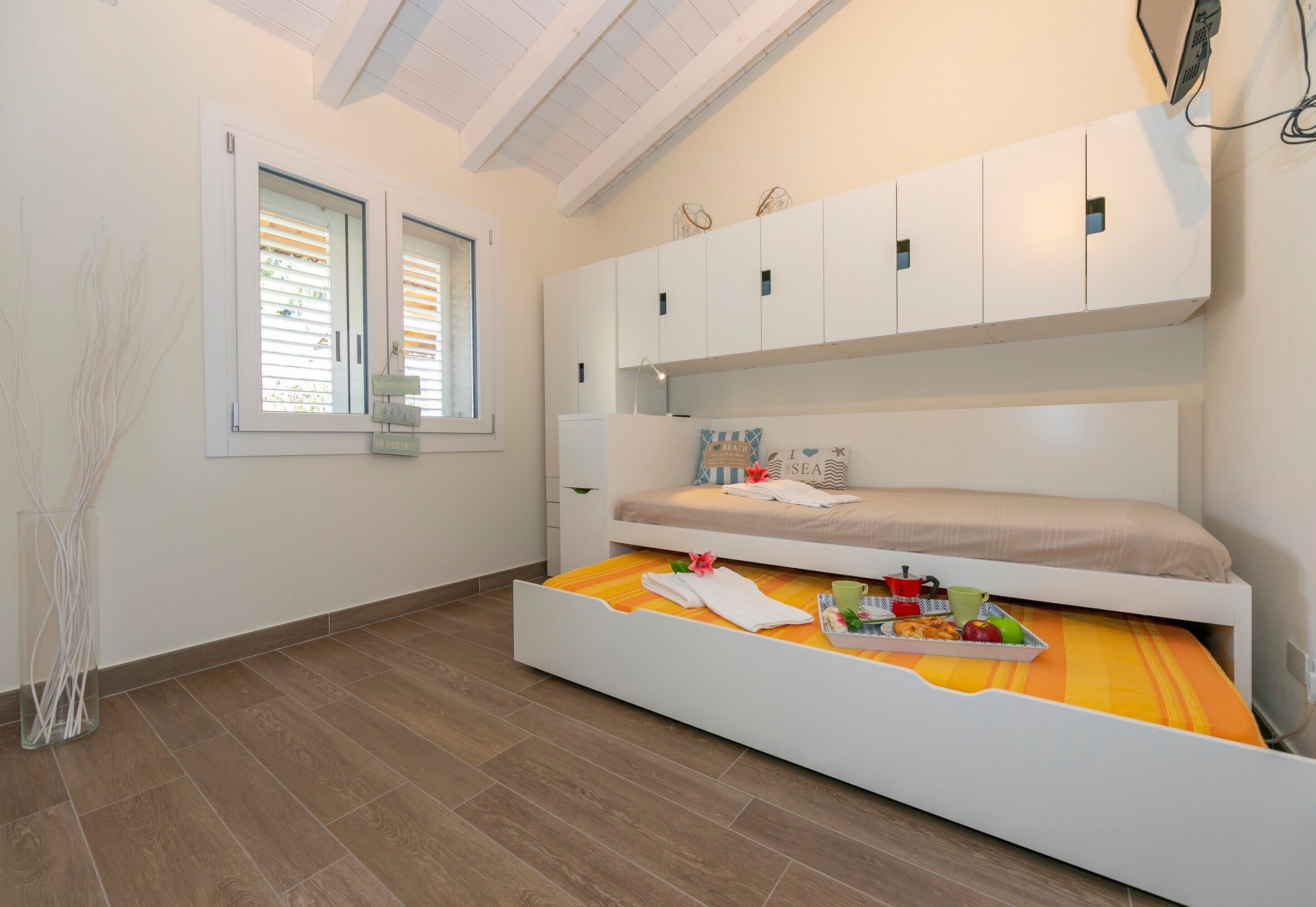 A bedroom with a bunk bed, a window with blinds, and a bedside table with a tray of fruits and a cup.