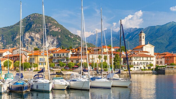 A marina with boats docked, a mountain in the background, and buildings with red roofs. - Villa Il Gelsomino Bellavista (Besozzo)