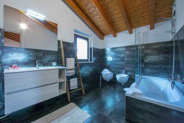 A modern bathroom with a large bathtub, a wooden ceiling, and a window providing natural light.