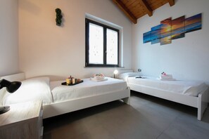 A room with two single beds, a desk, a window, and a wall-mounted painting.