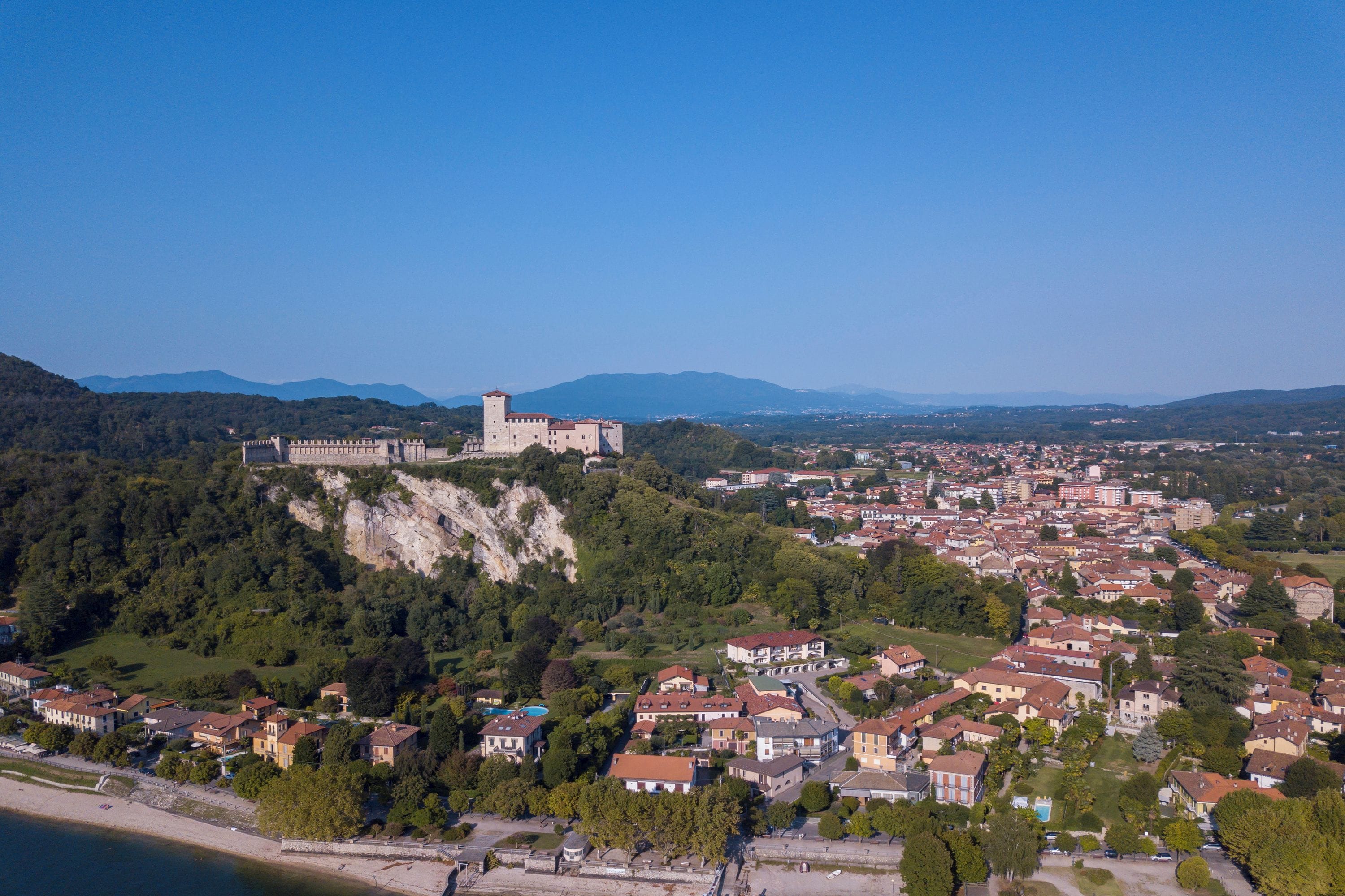 A coastal town with a prominent castle on a hill, surrounded by residential buildings and greenery.