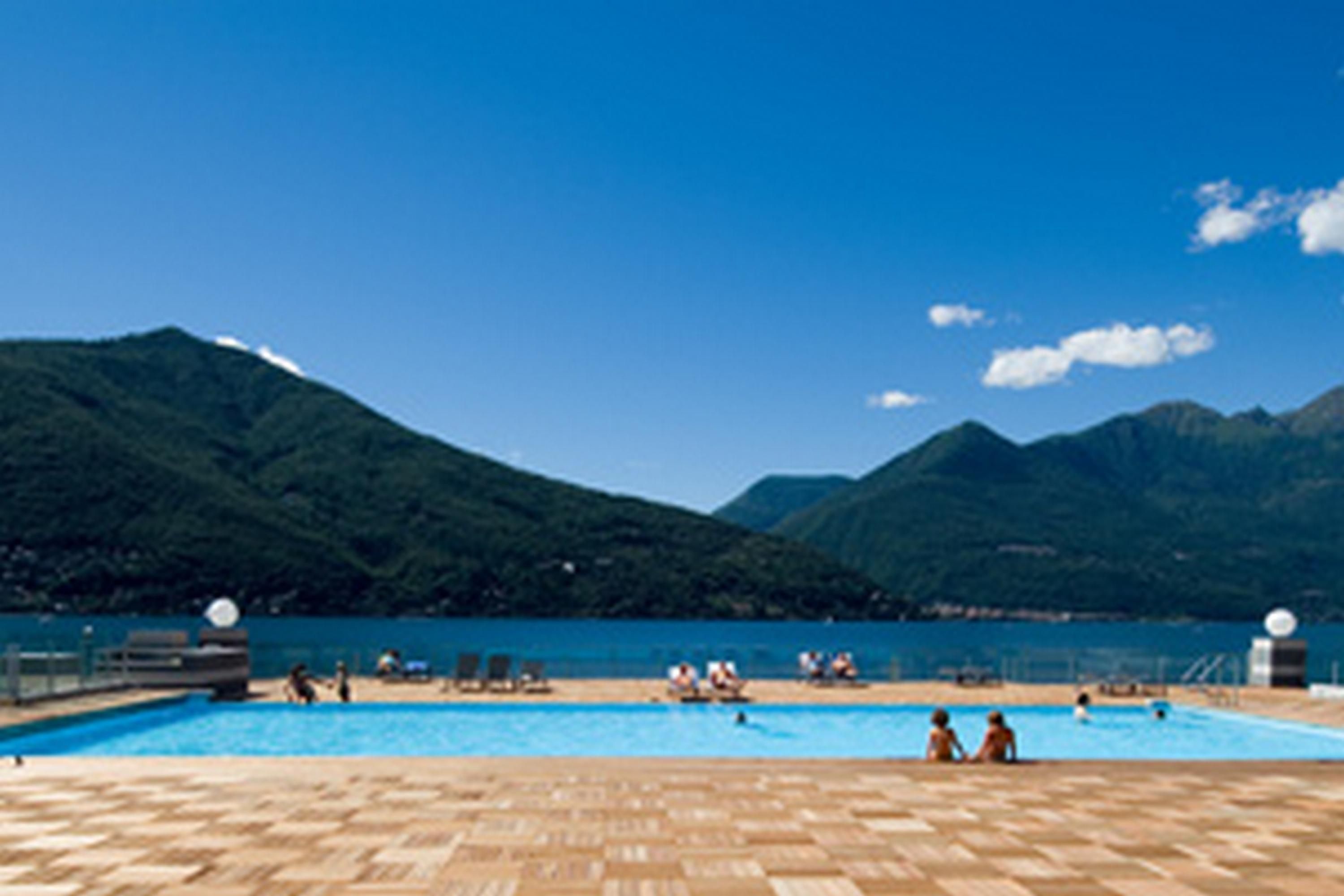 A swimming pool with people around it, surrounded by mountains and clear sky.