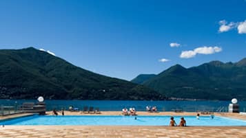 A swimming pool with people around it, surrounded by mountains and clear sky.