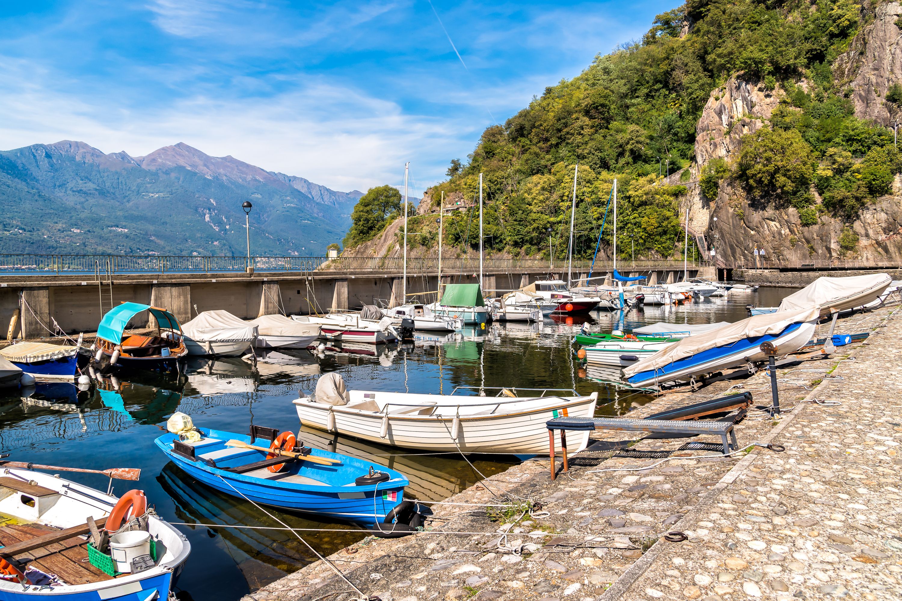 A marina with boats docked, a bridge in the background, and mountains in the distance.