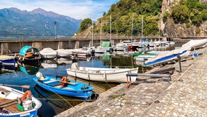 A marina with boats docked along a stone quay, surrounded by mountains and greenery.