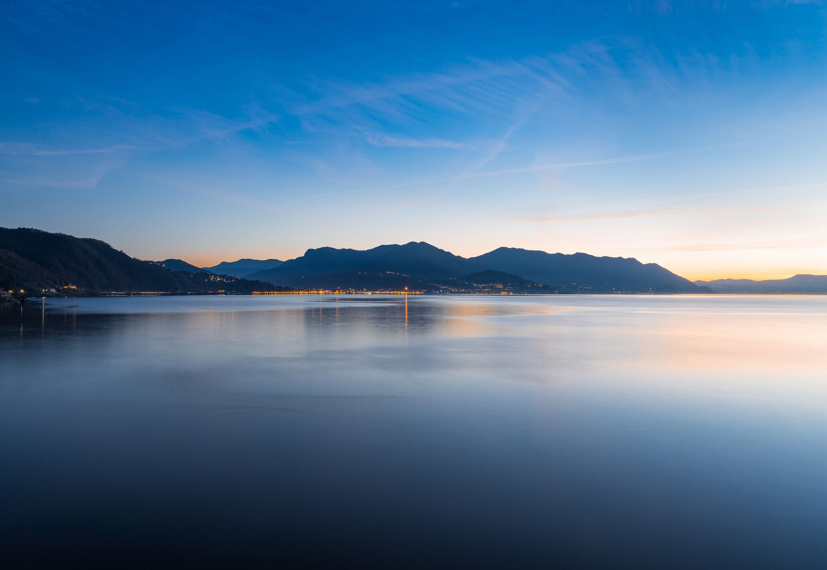 Ein ruhiger See mit Bergen im Hintergrund und einer Brücke in der Mitte.