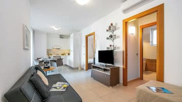 Una sala moderna con un sofá de cuero negro, un televisor sobre un mueble de madera y un comedor al fondo.