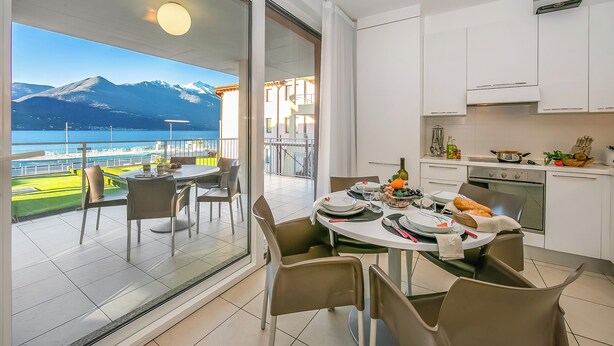 A modern kitchen with white cabinets and a dining area with a table set for two. A large window offers a view of mountains and a body of water.