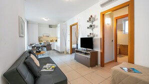 A modern living room with a black leather sofa, a TV on a wooden stand, and a dining area in the background.