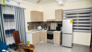 A compact kitchen with a stove, microwave, and refrigerator. There is a small dining area with a table and two chairs. - Kasa Nautica Homes & Comfort (Accra)