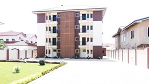 A multi-story residential building with a central vertical wooden panel, balconies, and a gated entrance. - Kasa Nautica Homes & Comfort (Accra)