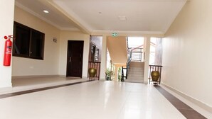 A spacious hallway with a fire extinguisher, a staircase, and a door. - Kasa Nautica Homes & Comfort (Accra)